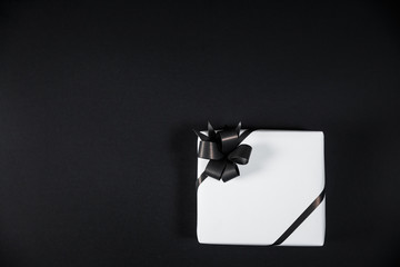 White gift box on a dark contrasted background, decorated with a textured bow, creating a romantic atmosphere.