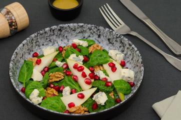 Fresh green salad with blue cheese and pomegranate. Spinach salad. Salad with spinach leaves, pears, blue cheese, pomegranate and walnuts, top view 
