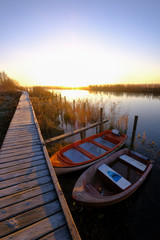 two boats at small harbor with wooden bridge and sunrise in backgrounds