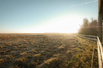 sunrise over a field with a fence on the right side of the picture