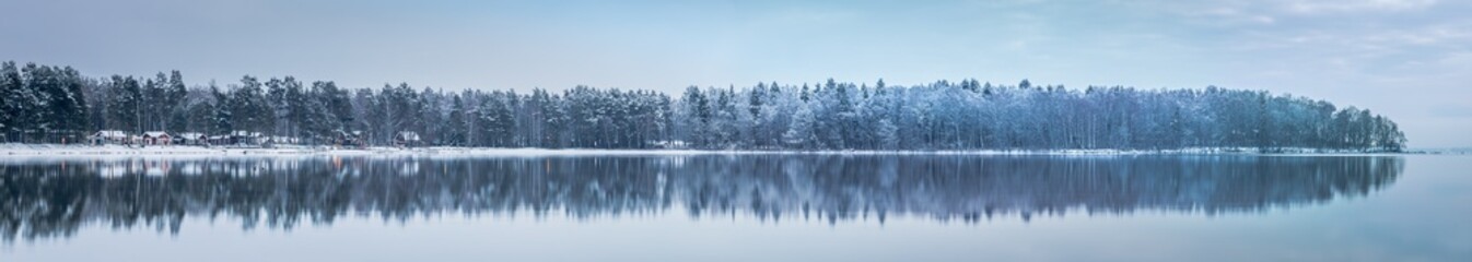 great panorama of winter forest with some small red houses reflected in a lake