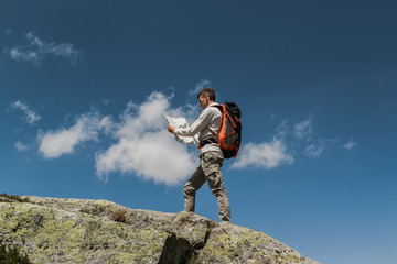 young man with big backpack walking to reach the top of the mountain during a sunny day. reading a map