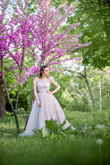 Luxurious and stylish bride poses in the garden among purple flowers. Happy bride with beautiful and long hair. An important day in life, strong emotions.