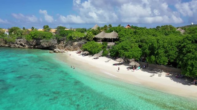 Aerial View Flying Past a Dock, Tourists, and a Straw Roof Hut on a Tropical Beach in Cura&radic;&szlig;ao of the Caribbean Islands, Bright Blue Crystal Clear Ocean Water