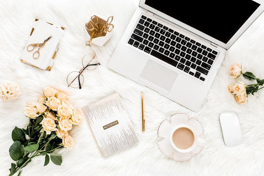 Female workspace with laptop, roses flowers bouquet, golden accessories, notebook, glasses. Flat lay women's office desk. Top view feminine background.
