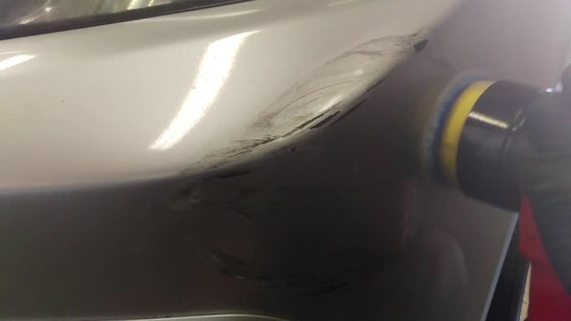 A man buffs out excessive paint damage on a car.