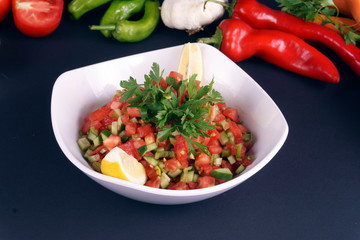 Green salad with fresh vegetables and green leaves at dark background.