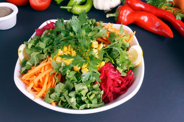 Green salad with fresh vegetables and green leaves at dark background.