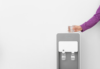 Woman with glass near water cooler on white background, closeup. Space for text