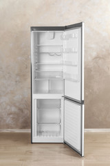 Open refrigerator with empty shelves near grey wall indoors