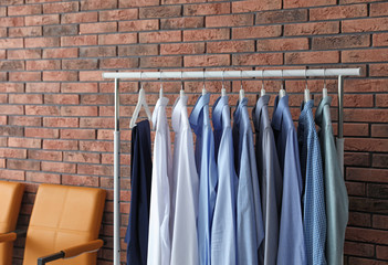 Wardrobe rack with men's clothes and chairs near brick wall