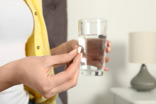 Woman with pill and glass of water indoors, closeup
