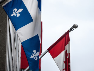 Quebec flag standing in front of the official flag of Canada in Montreal, the main city of Quebec, the second biggest province of Canada, French speaking, with specific relations to federal government