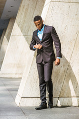 Young African American Businessman with beard, wearing black suit, leather shoes, standing by...