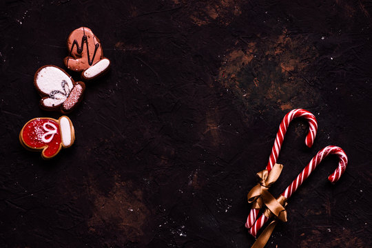 Decoration For New Year On Black Background. Gingerbread With Glaze In Form Of Mittens And Candy Canes. New Year's Treat. Christmas Sweets. Cook Yourself. Tea Biscuit. Gold,red Color.