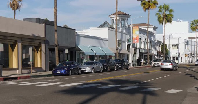 A daytime exterior establishing shot of traffic in the upscale shopping district near Rodeo Drive in Beverly Hills. Store names obscured for general stock use.  	