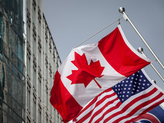 Canadian and USA flags in front of a business building in Toronto Ontario, Canada. Toronto is the biggest city of Canada, and one of the main economic and business hubs of North America - obrazy, fototapety, plakaty