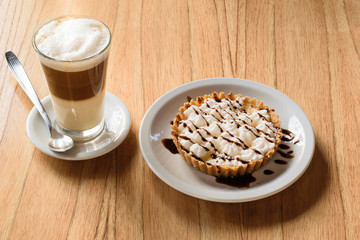 Cafe cappucchino en vaso largo sobre mesa de madera acompañado por  cake , torta , postre en vajilla blanca