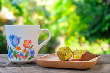 A cup of tea and red sweet potato on wooden plate over rustic wooden table