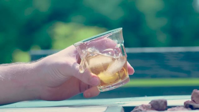 Man swirling, drinking and spilling whiskey bourbon rum on the rocks during warm summer day