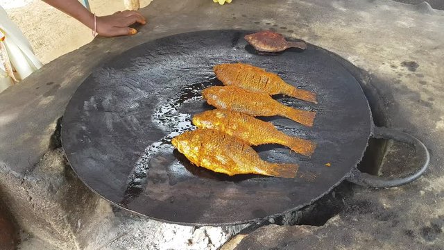A woman placing marinated spicy fish in a big cast iron pan and frying it