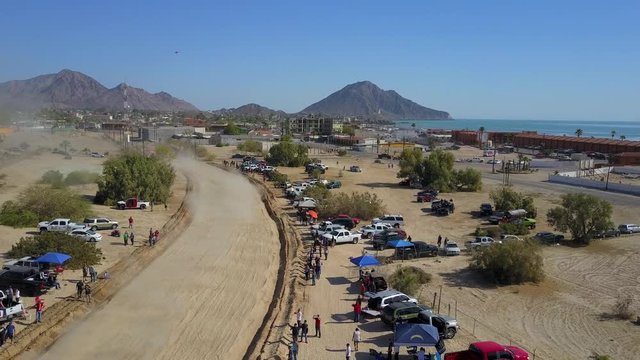 Aerial shot of the San Felipe 250 race. Green Trophy Truck races towards the camera and out of frame. Dust clouds rises behind the Truck