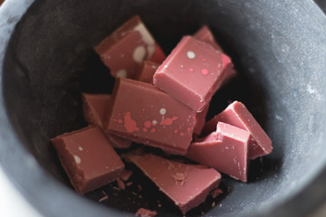 Broken and shattered pieces of ruby red chocolate in a round charcoal stone ceramic bowl. White and brwon background. Speckled chocolate.