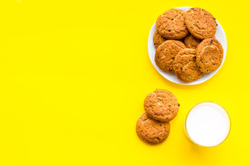 Drink milk with cookies concept. Cup of milk and fresh homemade cookies on yellow background top view copy space