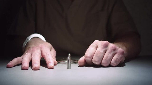 Close-up of a prisoner's hands while he sits calmly handcuffed to a table in an interrogation room.