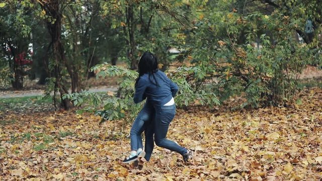 Happy mother and her Little daughter having fun in autumn park. Young family throwing leaves and laughing. Slow-motion