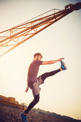 Young man exercising outdoors by the crane at sunset