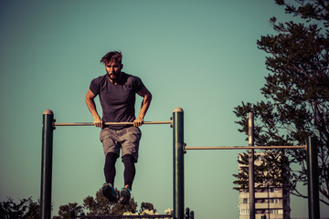 Fototapeta premium Young man exercising on gymnastic bar in park at morning