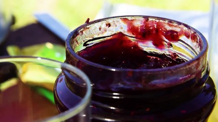 Taking a spoon of strawberry marmelade and drinking a orange juice during a outdoor breakfast or brunch