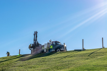 Fototapeta premium Caucasian male Engineers working and operating a hydraulic telescopic truck mounted auger crane drill rig on a hill on a sunny summer day. Professional team of men hard at work in the field.