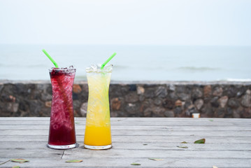 Juice mix berry, mango and passion fruit drink in tall glass with straw green color on wooden terrace front of sea