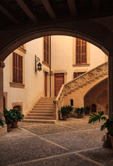 Old terracotta colored inner courtyard with a large staircase seen through a dark archway in a residential neighborhood in Palma de Mallorca in Mallorca on Balearic islands in Spain © SvetlanaSF