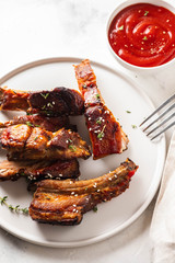 Bbq pork ribs with chili sauce on white plate. Pork ribs on slate background. Copy space.