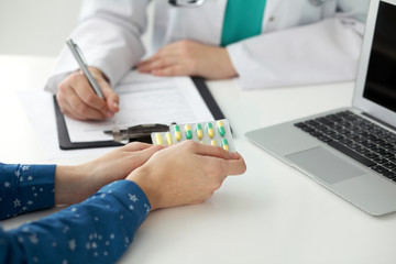  Close-up of a doctor and  patient  sitting at the desk while physician filling up medical history form. Medicine and health care concept