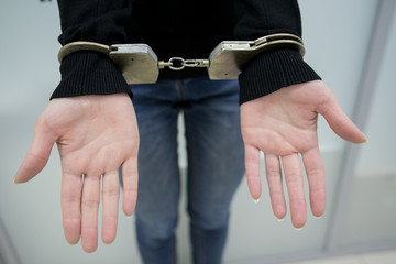 Close-up. Arrested man handcuffed hands at the back isolated on gray background. Prisoner or...