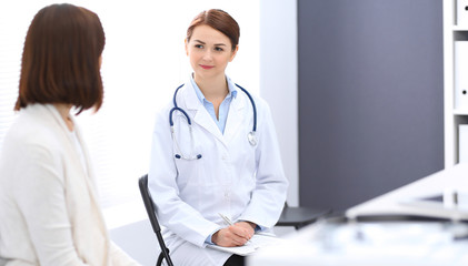 Fototapeta premium Happy doctor and patient discussing something while sitting at the chairs at hospital. Physician at work in clinic. Medicine and healthcare concept
