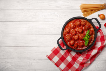 Meatballs in tomato sauce with spices and basil in a frying pan on a white wooden board