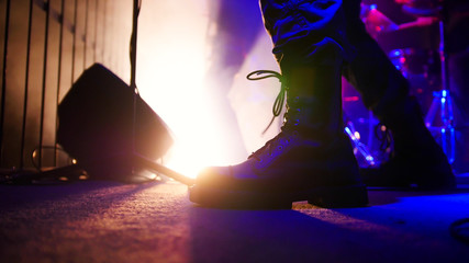 Rock concert. Guitarist in black massive boots playing guitar. Feet close up