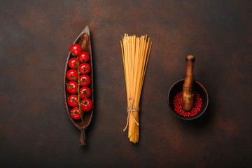 Cherry tomatoes twig on a wooden figure plate with pasta mortar and red pepper on rusty brown...