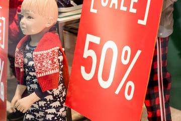 red sale sign in kids clothes shop window next to a mannequin dressed in winter clothes.Winter sale.Children clothing store. Fashionable brand of clothing and accessories window display in Merry
