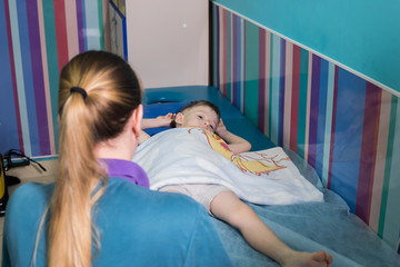 Medical clinic. An occupation with child with cerebral palsy. A nurse standing in front of the baby