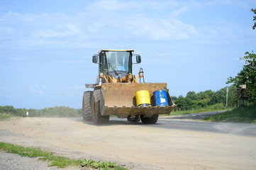 A large yellow wheeled tractor with a bucket carries two tanks on the highway. Transportation of cargo, construction