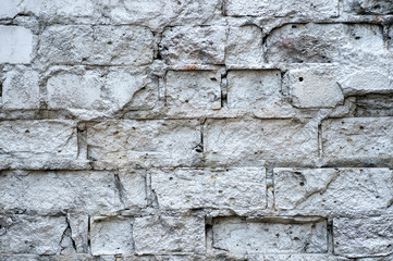 The white wall with the hollows in the bricks with cracks and cement mortar between them. Background