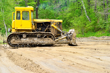 Tractor on tracks with a bucket on clearing the shoreline for the construction of beach volleyball courts.
