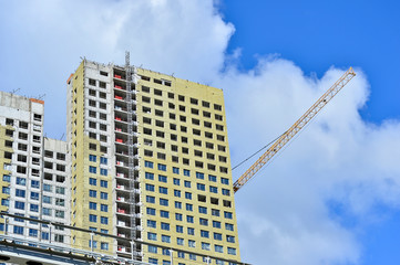 Construction of a high-rise building against a blue sky with clouds. Bottom view. In the foreground of the ground branch of the subway