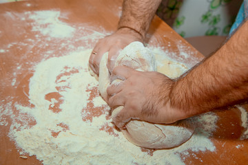 A man on the kitchen table kneads the dough for baking.